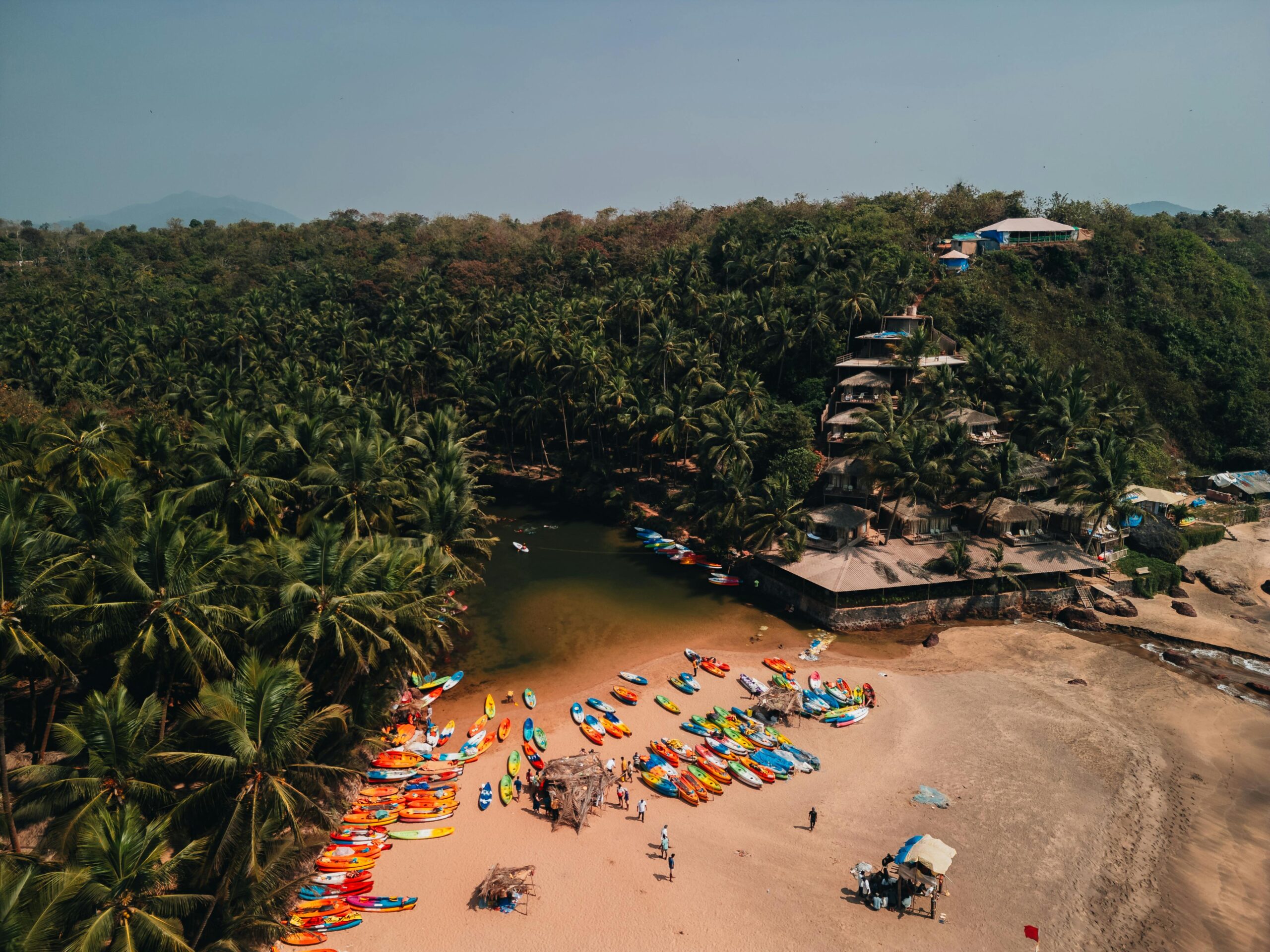Explore the vibrant kayaks and serene beach backdrop at Sacral Beach, Goa, from a captivating aerial perspective.