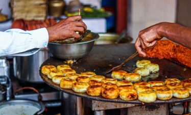 Close-up of a street vendor preparing traditional fried snacks on an outdoor grill.