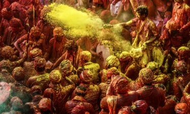 Crowd celebrating Holi festival with colorful powders in vibrant outdoor setting.