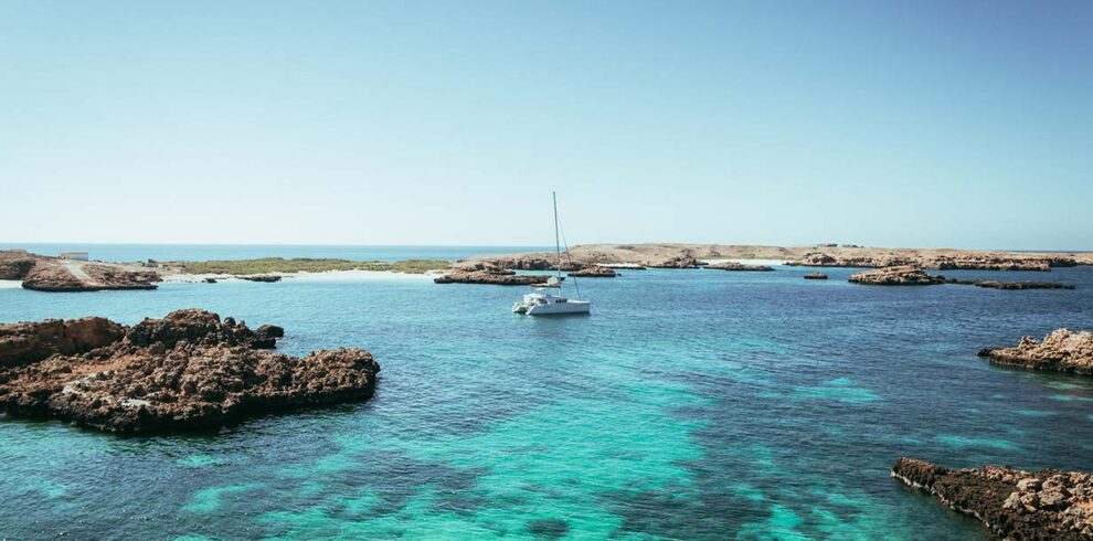 Un catamarano bianco ancorato nelle acque turchesi e trasparenti della riserva naturale delle Isole Daymaniyat in Oman.
