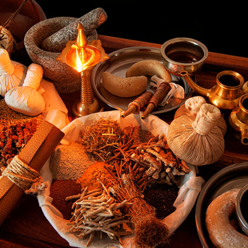 Accessori per trattamenti ayurvedici disposti con cura, tra cui ciotole di rame, oli alle erbe e sacchetti di polveri medicinali.