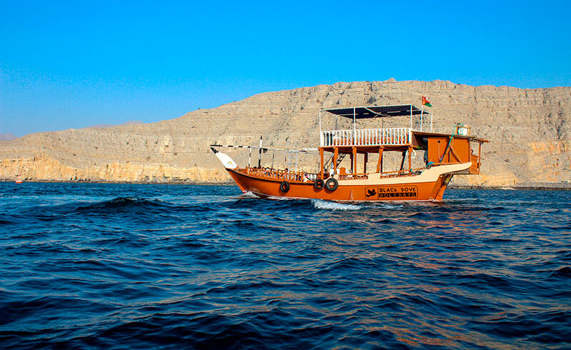 Una tradizionale imbarcazione dhow in legno che naviga tra i maestosi fiordi di Khasab nella penisola del Musandam, Oman.