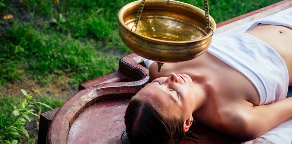 Massaggio terapeutico ayurvedico completo eseguito con oli caldi su un tavolo tradizionale in legno da terapisti professionisti.