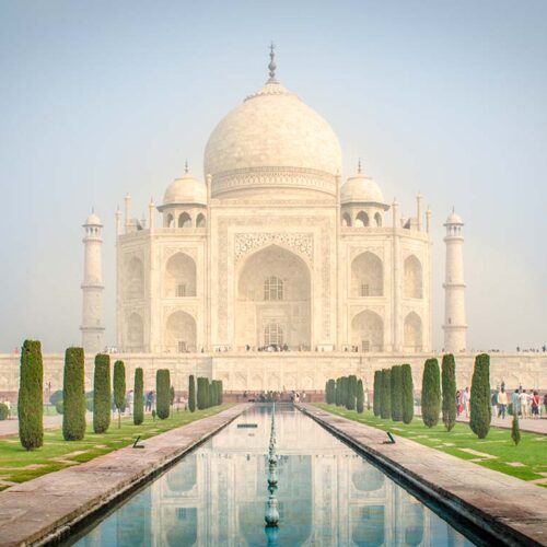 Il maestoso mausoleo in marmo bianco del Taj Mahal di Agra riflesso nei canali d'acqua dei giardini monumentali, India.