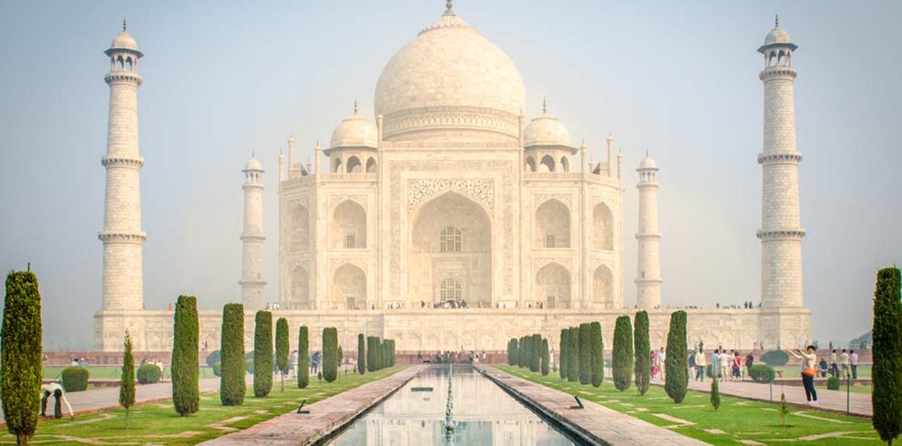 Il maestoso mausoleo in marmo bianco del Taj Mahal di Agra riflesso nei canali d'acqua dei giardini monumentali, India.