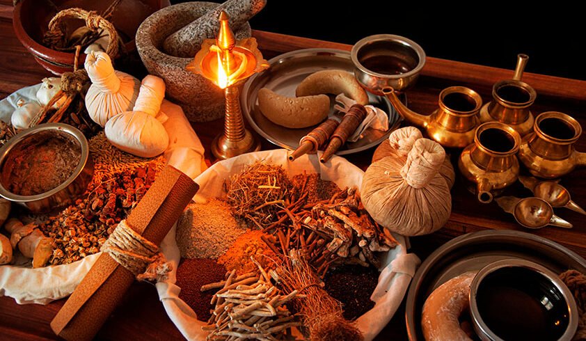 Een selectie van traditionele ayurvedische accessoires, waaronder kruidenstempels, gedroogde kruiden, oliën, een vijzel en een brandende koperen olielamp
