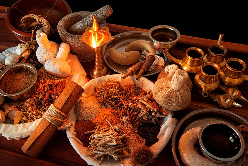Een selectie van traditionele ayurvedische accessoires, waaronder kruidenstempels, gedroogde kruiden, oliën, een vijzel en een brandende koperen olielamp
