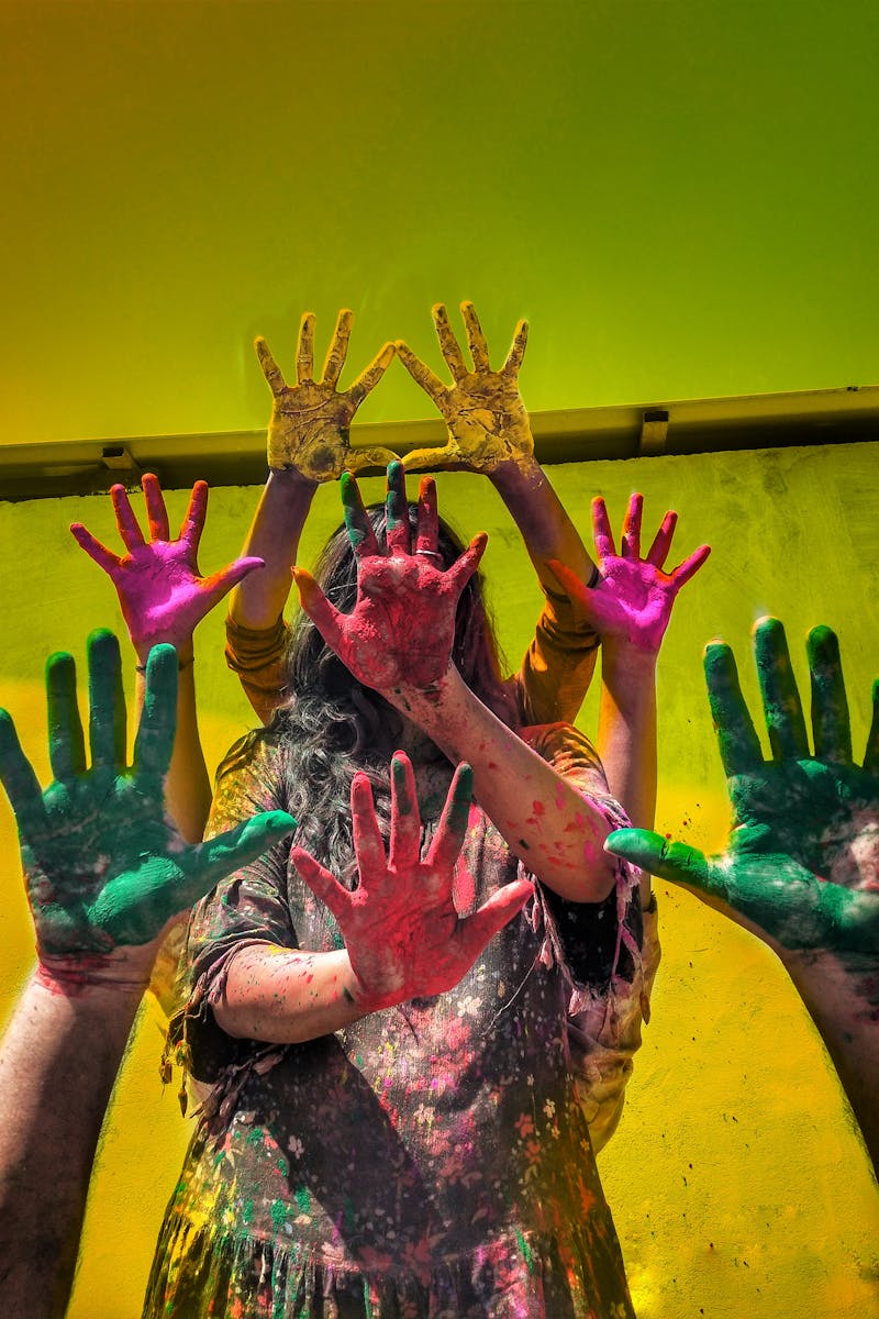 Group of people celebrating Holi with colorful painted hands and vibrant background.