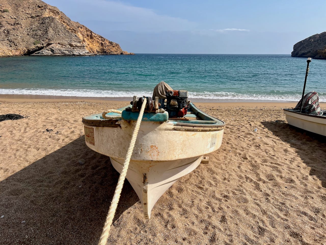 Tranquil view of a boat on the sandy beach of Bandar Al Khairan, Oman, with rocky coastline and blue sea.