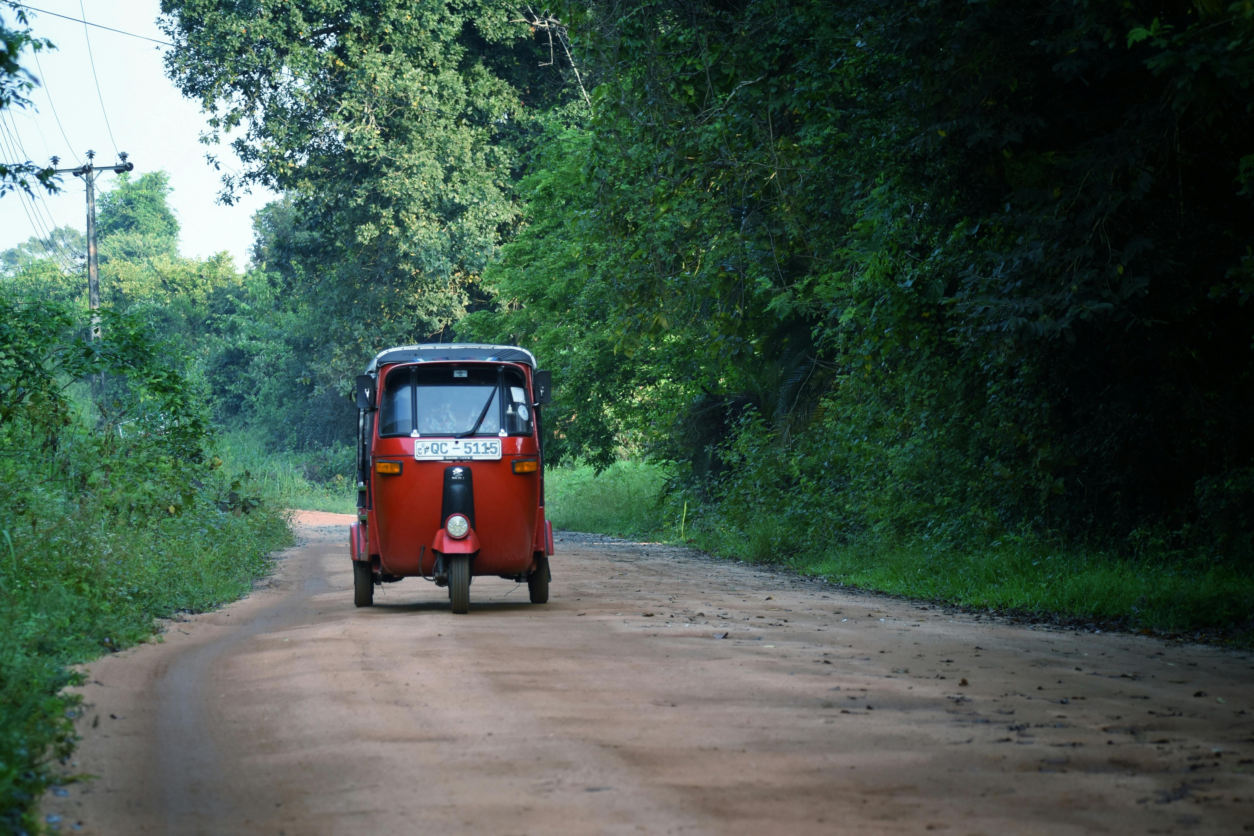 A red tuk tuk travels down a peaceful rural road in scenic Sigiriya, Sri Lanka.