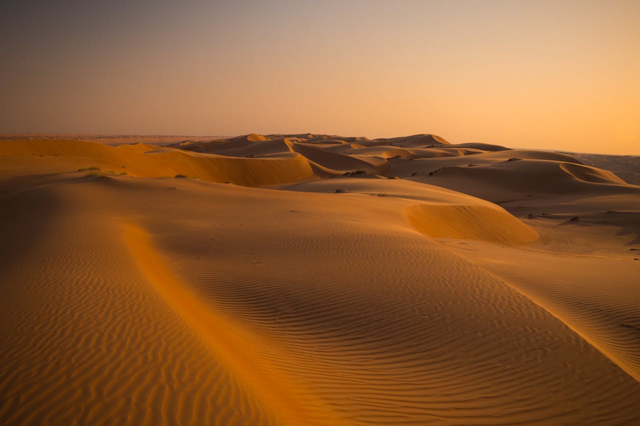Captivating golden sand dunes under a soft sunset in the vast desert landscape of Oman.