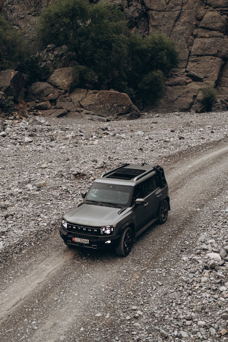 Aerial view of an SUV navigating a rugged, rocky path in the scenic landscapes of Oman.