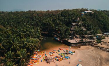 Explore the vibrant kayaks and serene beach backdrop at Sacral Beach, Goa, from a captivating aerial perspective.