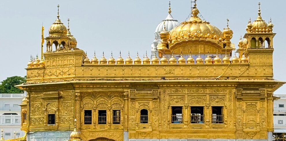Stunning view of the Golden Temple reflecting in water on a sunny day in Amritsar, India.