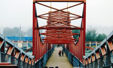 People walking across a red steel bridge in Haridwar, India, showcasing modern infrastructure.