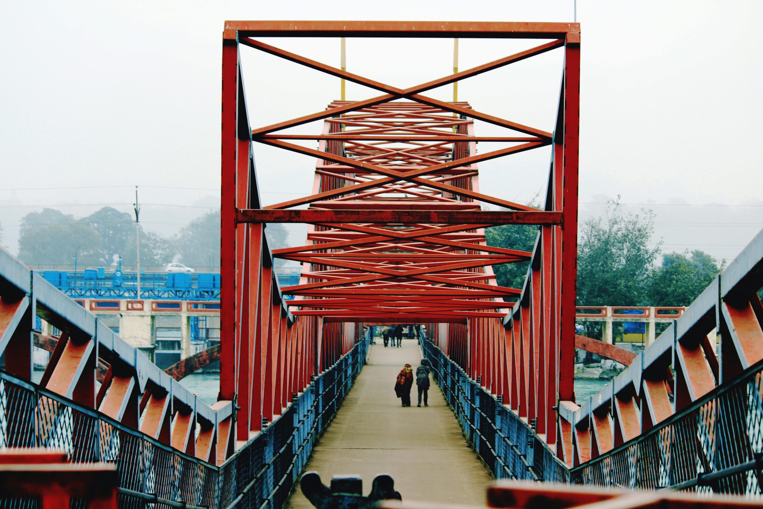 People walking across a red steel bridge in Haridwar, India, showcasing modern infrastructure.