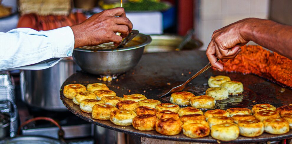 Close-up of a street vendor preparing traditional fried snacks on an outdoor grill.