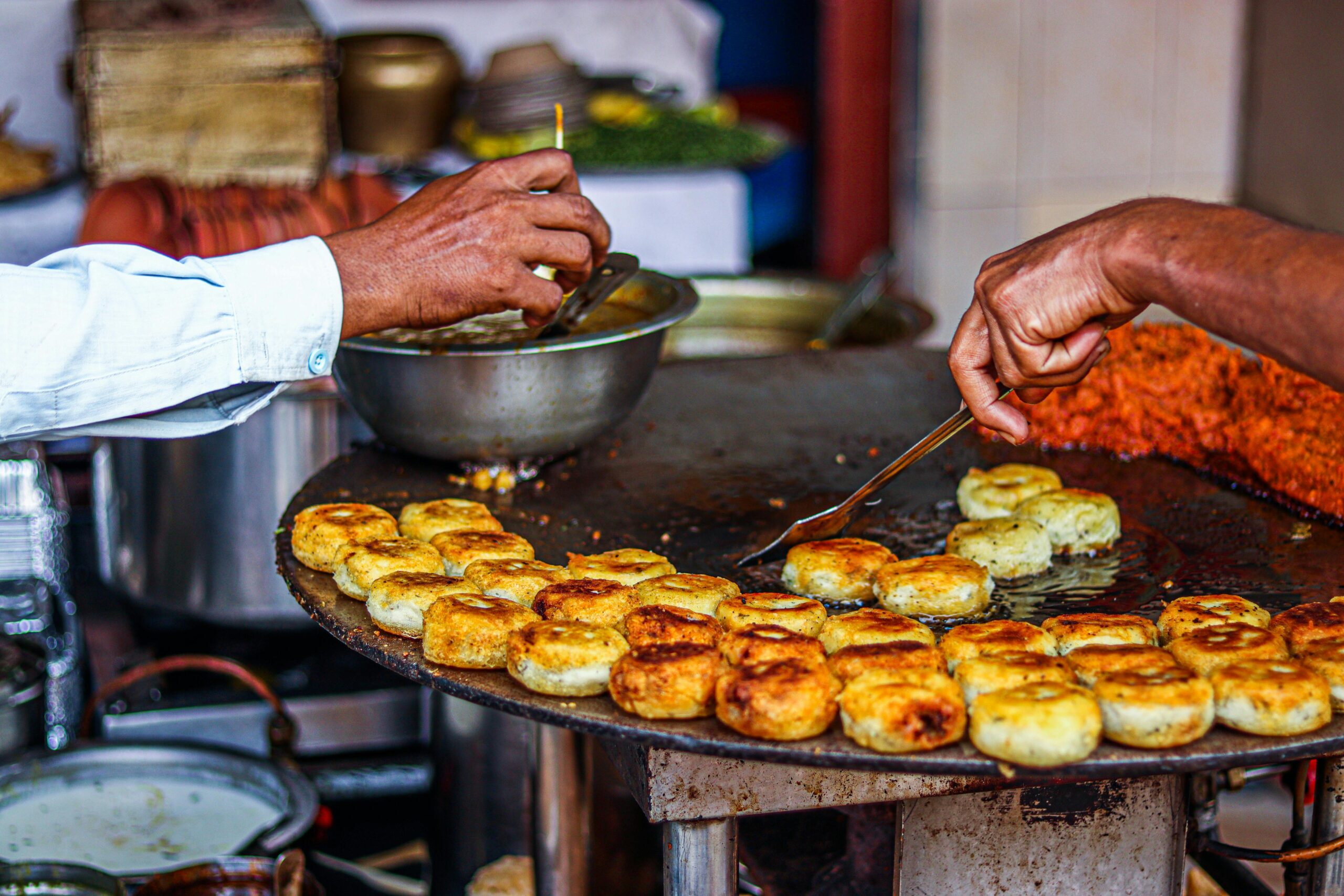 Close-up of a street vendor preparing traditional fried snacks on an outdoor grill.