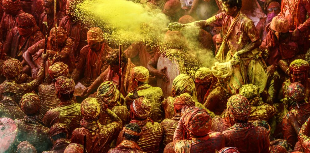 Crowd celebrating Holi festival with colorful powders in vibrant outdoor setting.